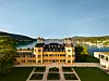 Falkensteiner Schlosshotel Velden uz jezero, s vrtovima, šumovitim brežuljcima i planinama u pozadini.