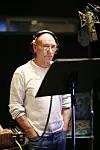 Patrick Stewart u bijeloj majici i slušalicama za mikrofonom u studiju za snimanje filma TMNT.