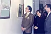 Muškarac u kariranom odijelu i posjetitelji razgledavaju slike u galeriji.