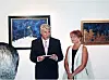 Muškarac u crnom odijelu i žena u svijetloj haljini stoje u galeriji uz apstraktne slike.