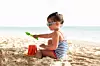 Side View Of A Little Girl Building Sand Castle With Plastic Bucket On Beach