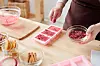 Hands of female sprinkling dry grated floral petals on top of pink handmade soap bars in silicone molds during master class
