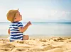 The cute baby boy playing on the beach. Little boy sitting on the sand. Sea and seashore as background with copy space